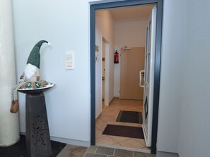 Un passadís amb una porta que dona a una habitació, una petita estàtua sobre un pedestal i un extintor fixat a la paret.