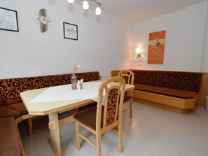 Un'area pranzo con tavolo in legno, sedie e una panca. Sono presenti orologi a parete e un quadro incorniciato.
