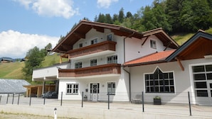 Um edifício de vários andares com telhado inclinado, sacadas e um estacionamento cercado.