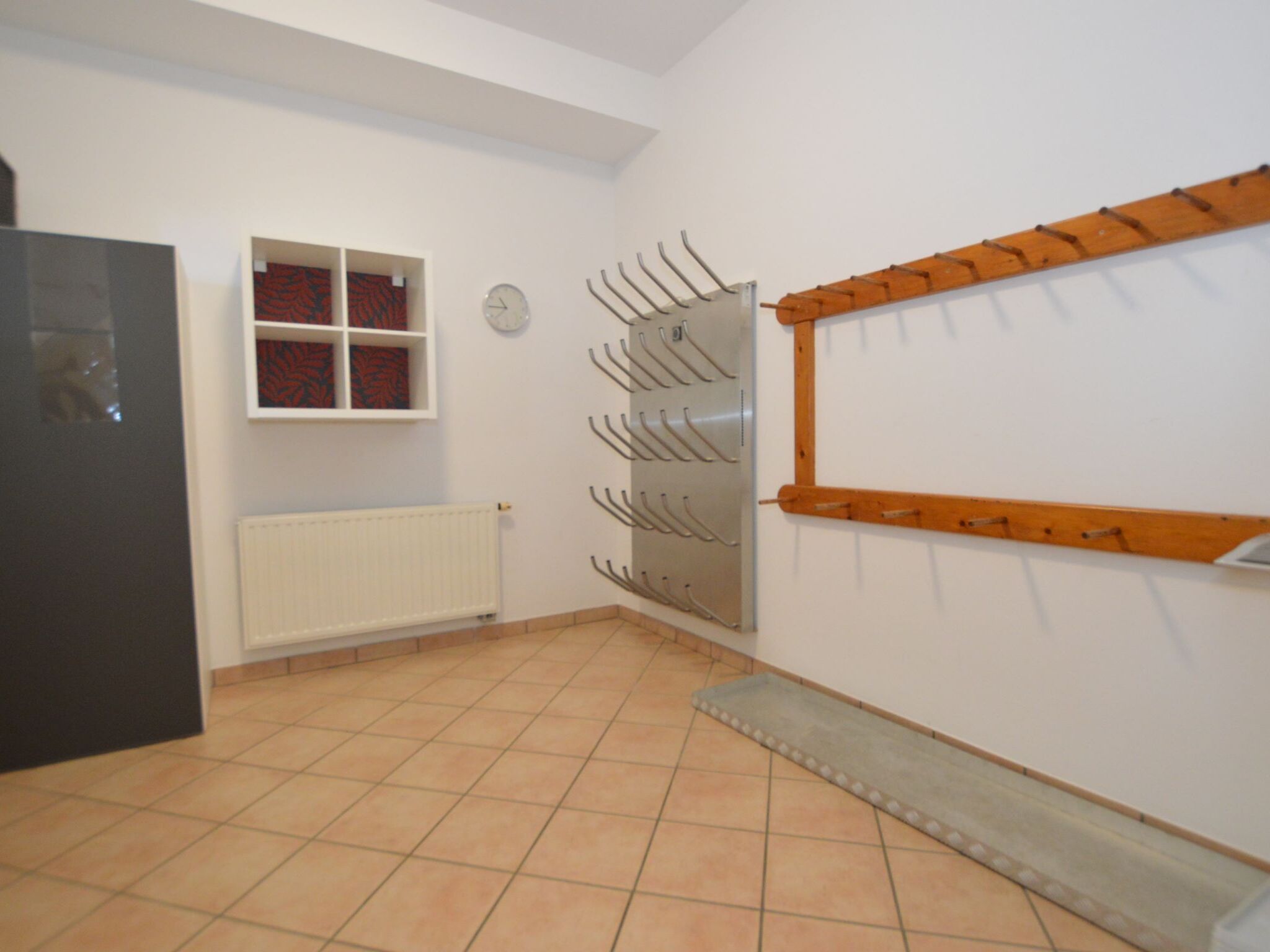 A room with a tiled floor, a radiator, a window with red curtains, and a wall-mounted coat rack.