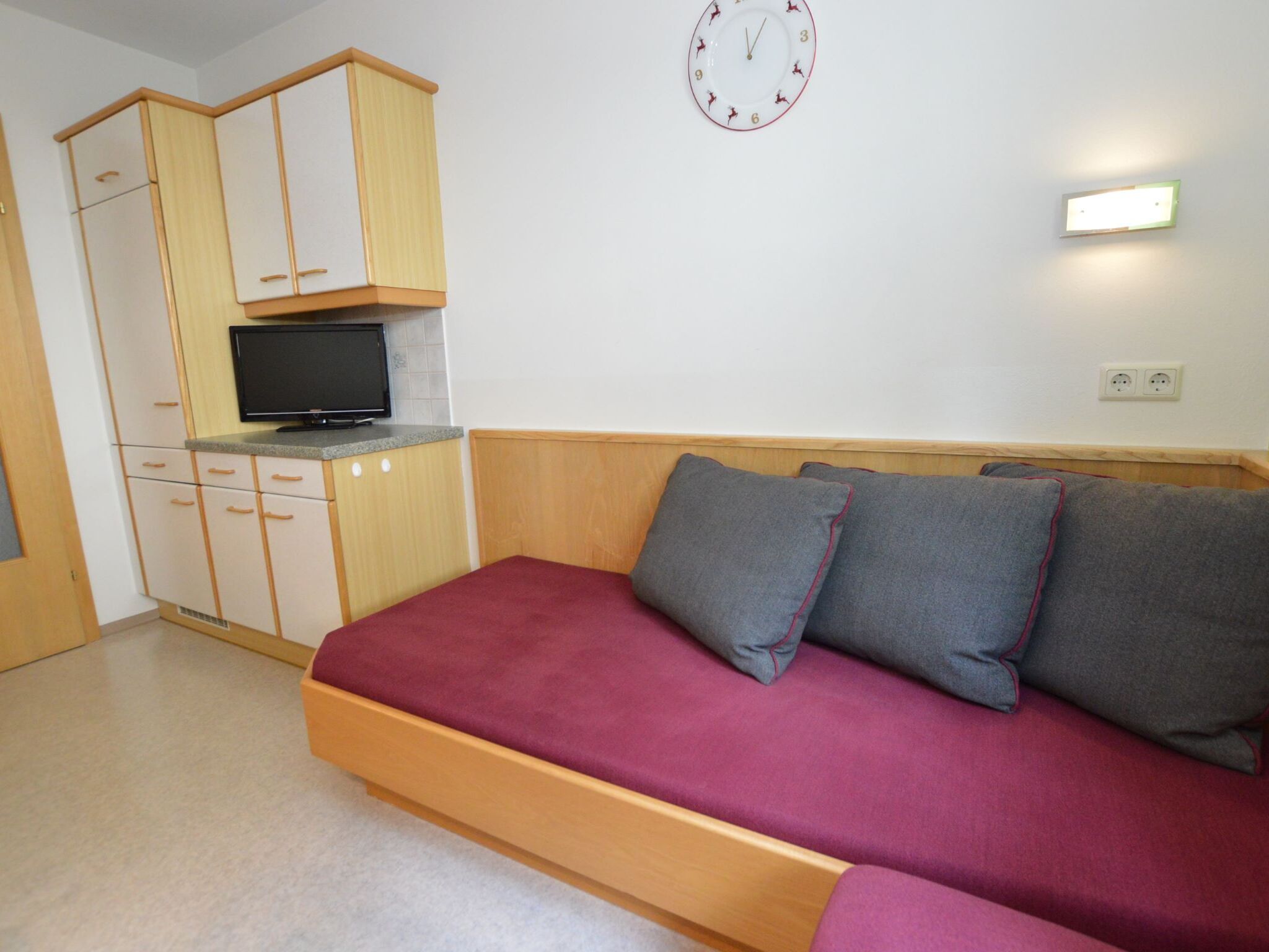 A compact room with a bed, a television, and a wall clock.