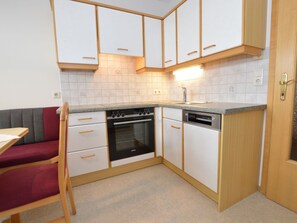 A compact kitchen with white cabinets, a built-in oven, a dishwasher, and a small dining area with a red chair. - House with last ski descent around the corner (Wagrain)