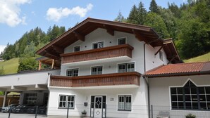 A multi-story building with a balcony, a sign indicating the number 19, and a parking area with cars. - A warm nest as your home in the mountains (Wagrain)