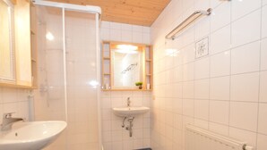 A bathroom with a white sink, a mirror, a shower, and a tiled floor. - A warm nest as your home in the mountains (Wagrain)