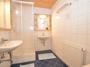 Une salle de bain avec un lavabo blanc, un miroir, une douche et un sol carrelé.