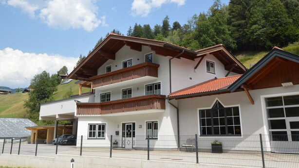 A multi-story building with balconies, a garage, and a fenced parking area. - A warm nest as your home in the mountains (Wagrain)