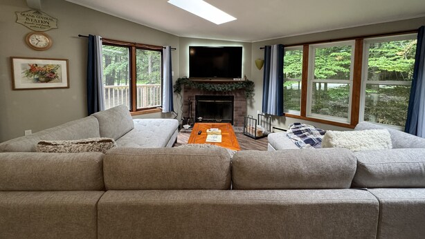 Una sala de estar con chimenea, un conjunto de sofás, una mesa de centro y ventanas grandes.