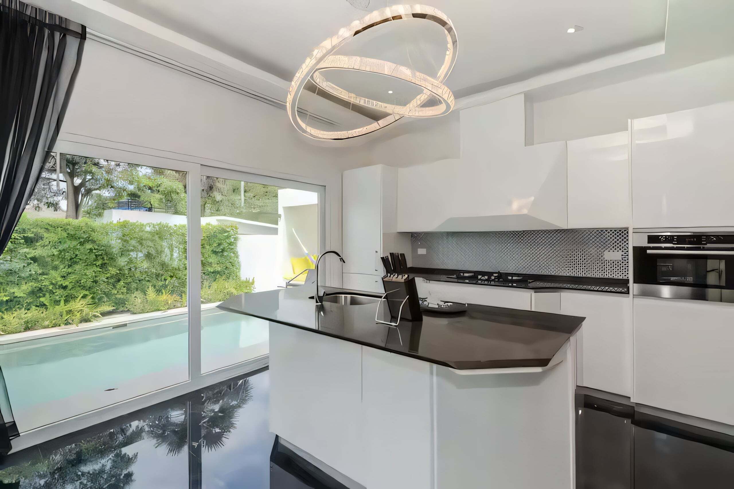 Een moderne keuken met een glazen kookeiland, roestvrijstalen apparatuur en uitzicht op een zwembad.