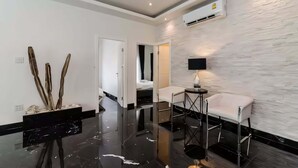 Quarto de hotel moderno com piso preto brilhante, sofá branco, mesa pequena e ar-condicionado fixado na parede.
