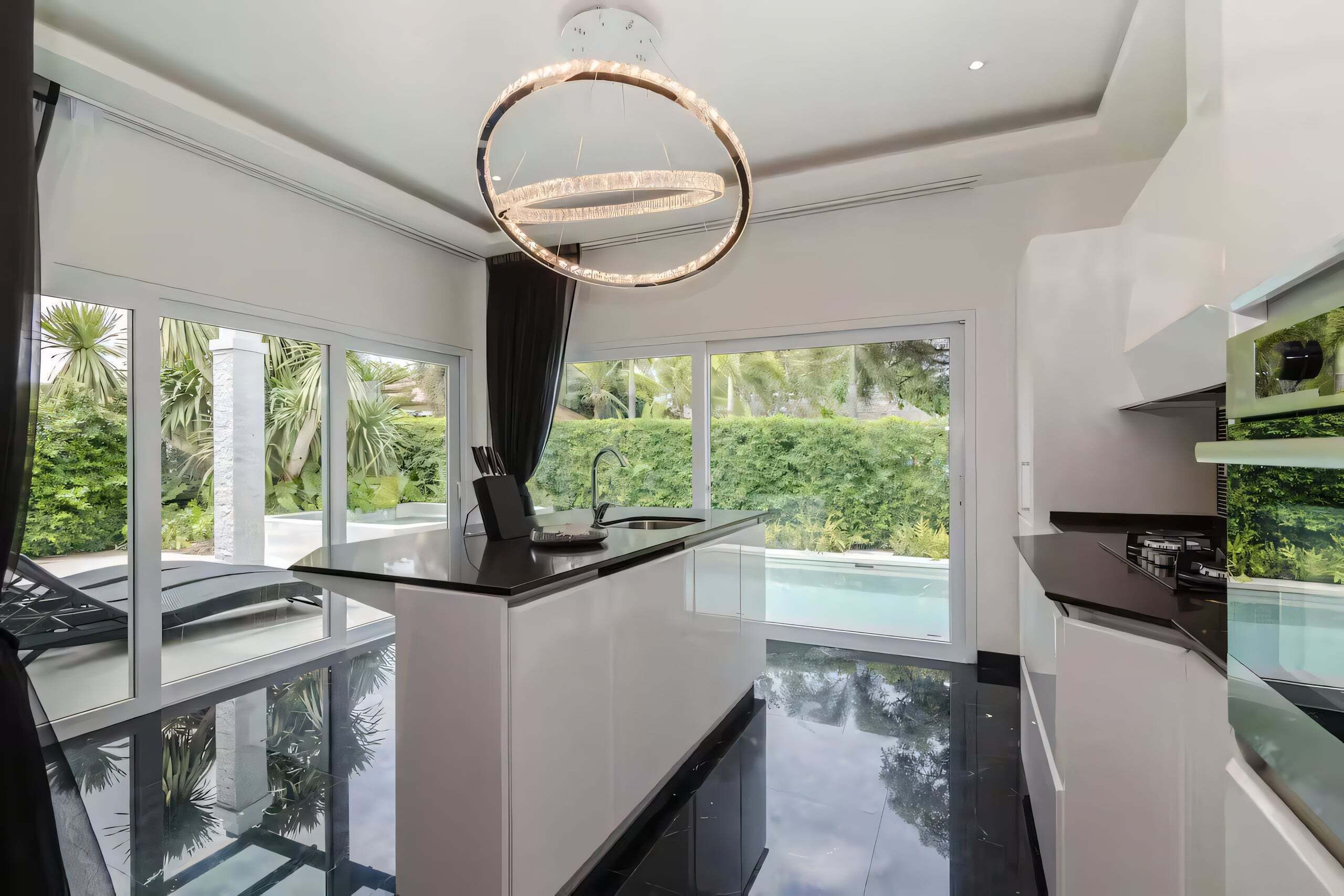 A modern kitchen with a central island, large windows, and a view of a swimming pool.