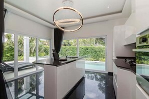 Une cuisine moderne dotée d’un îlot central, de grandes fenêtres et d’une vue sur une piscine.