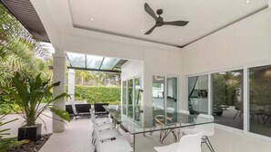 Um interior moderno com mesa de jantar de vidro, cadeiras brancas e ventilador de teto.