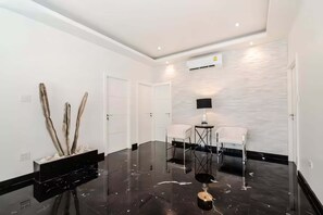 A modern interior with a polished floor, a white wall with a textured pattern, and a black-framed table with two chairs. - Orchid Paradise Homes OPV 03 (Tambon Hua Hin)