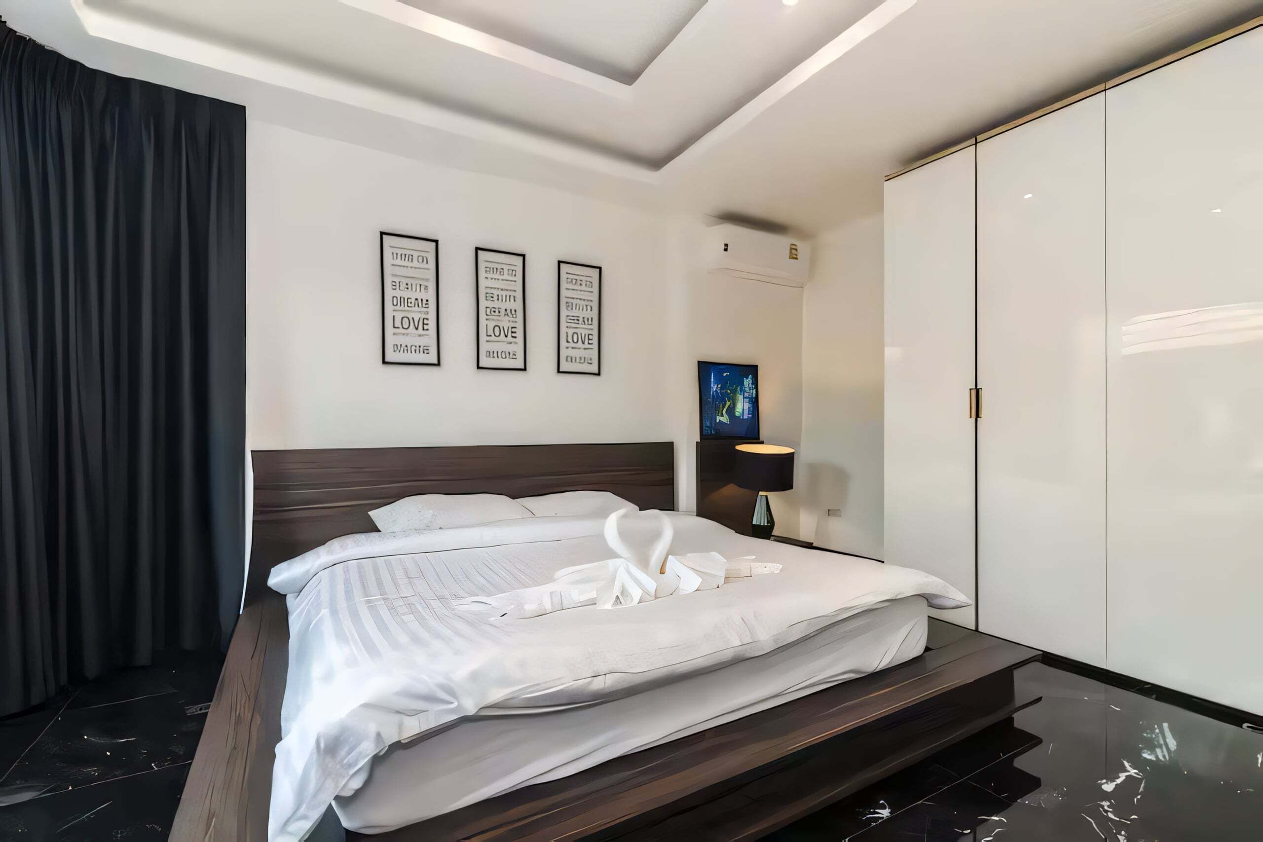 Quarto de hotel moderno com uma cama grande, um guarda-roupa e uma TV fixada na parede.