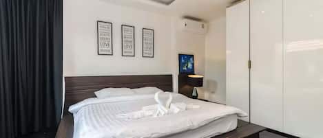 A modern hotel room with a large bed, a wardrobe, and a wall-mounted TV.