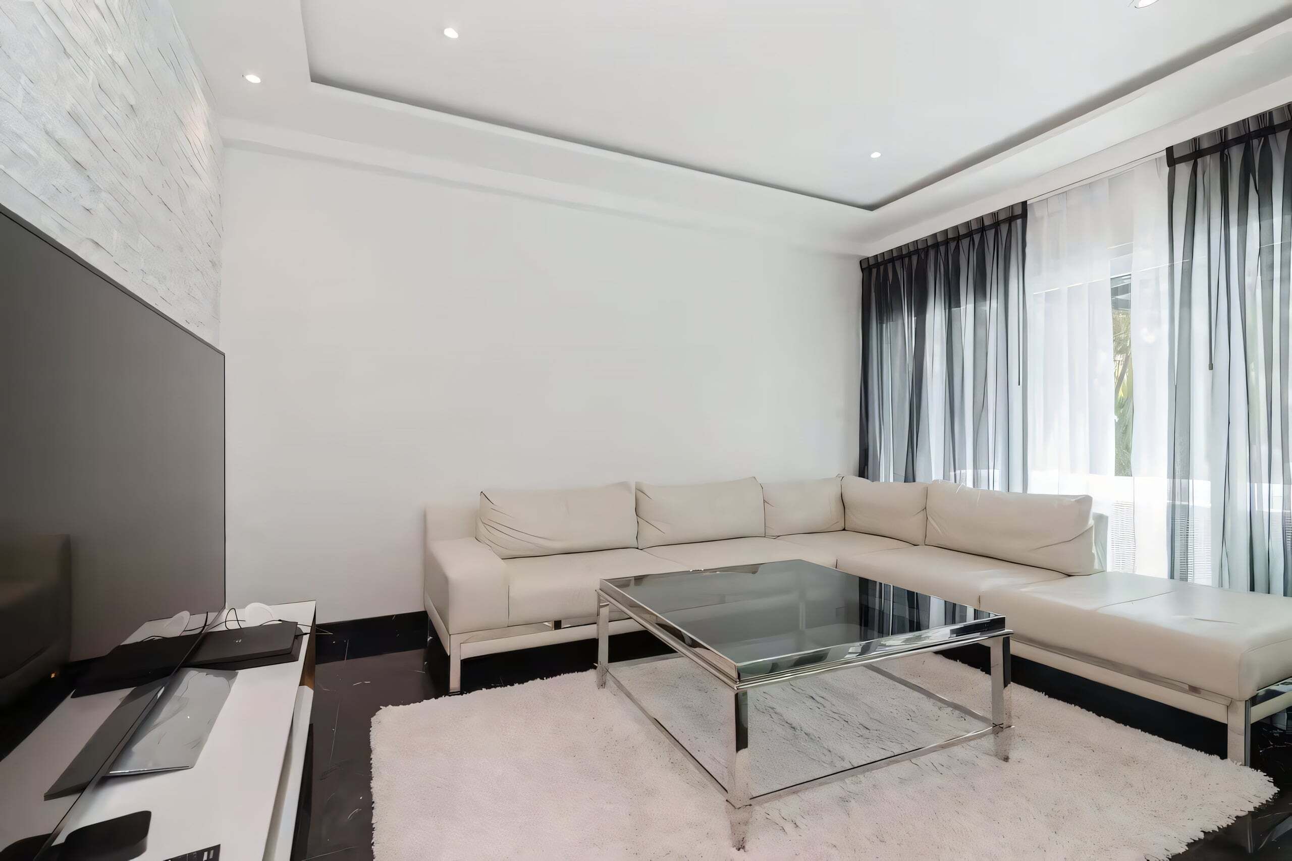 Uma sala de estar moderna com um sofá de canto, uma mesa de centro de vidro e uma televisão de tela plana grande.