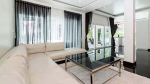 Uma sala de estar moderna com um sofá, uma mesa de centro de vidro e janelas amplas com cortinas.