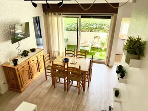 A dining area with a wooden table and chairs, a TV mounted on the wall, and a sliding glass door leading to an outdoor space. - Penon · 2 ch · Plage à pied, vélo, calme & repos (Seignosse)