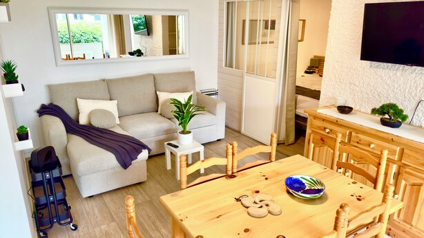 Ett modernt vardagsrum med en soffa, ett matbord med stolar, en tv som är monterad på väggen och en skjutdörr som leder till ett annat rum.