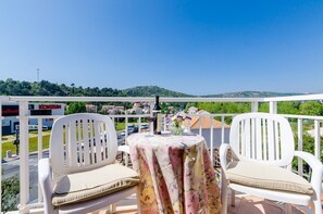 A balcony with two white chairs and a table, overlooking a street with buildings and a hill in the distance. - Pansion Srebreno - Double or Twin Room With Balcony and City View 3 (Zupa dubrovacka)