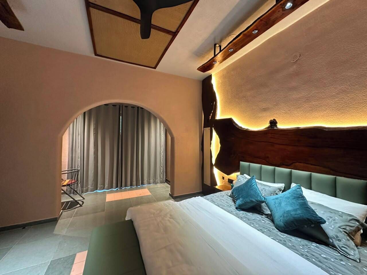 Un dormitorio con cama, cabecera y ventana con cortinas.