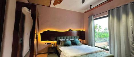 Un dormitorio con cama, mesitas de noche, un banco, ventilador de techo y ventana con cortinas.