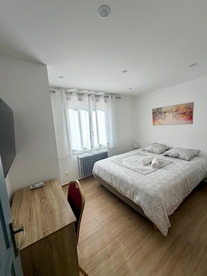 A bedroom with a bed, a desk, a chair, a radiator, a window with curtains, and a painting on the wall.