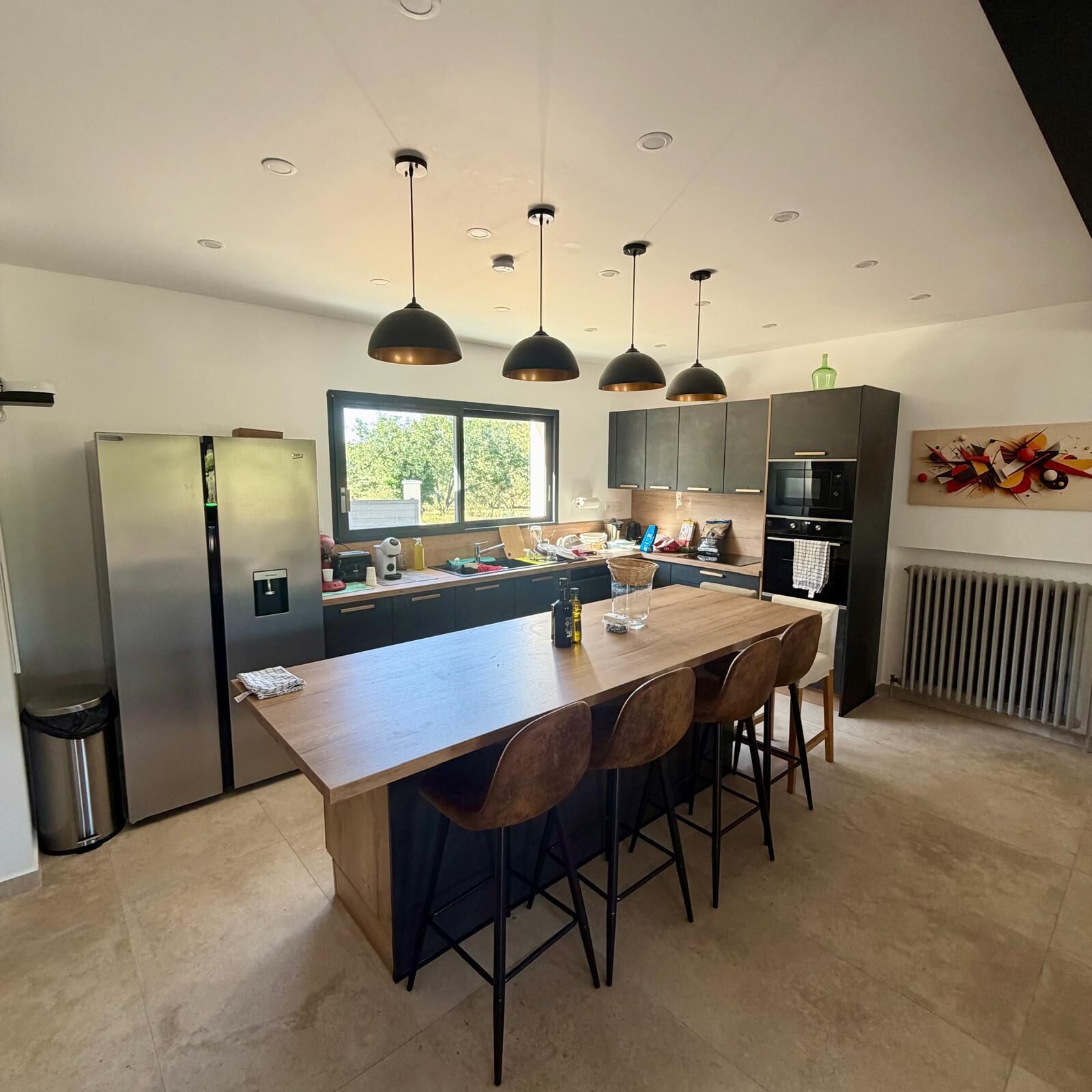 A modern kitchen with a central island, pendant lighting, and a view of the outdoors.