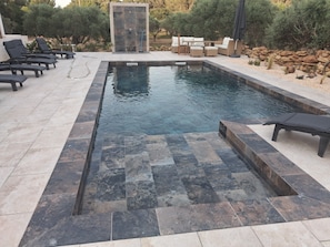 A rectangular swimming pool with a stone border, surrounded by lounge chairs and a seating area.