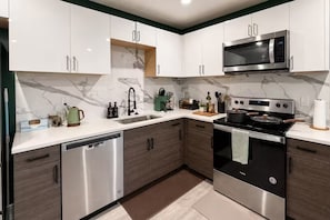 A modern kitchen with white cabinets, a stainless steel dishwasher, a built-in microwave, and a black stove. - Biophilic Oasis Knox Henderson (Dallas)
