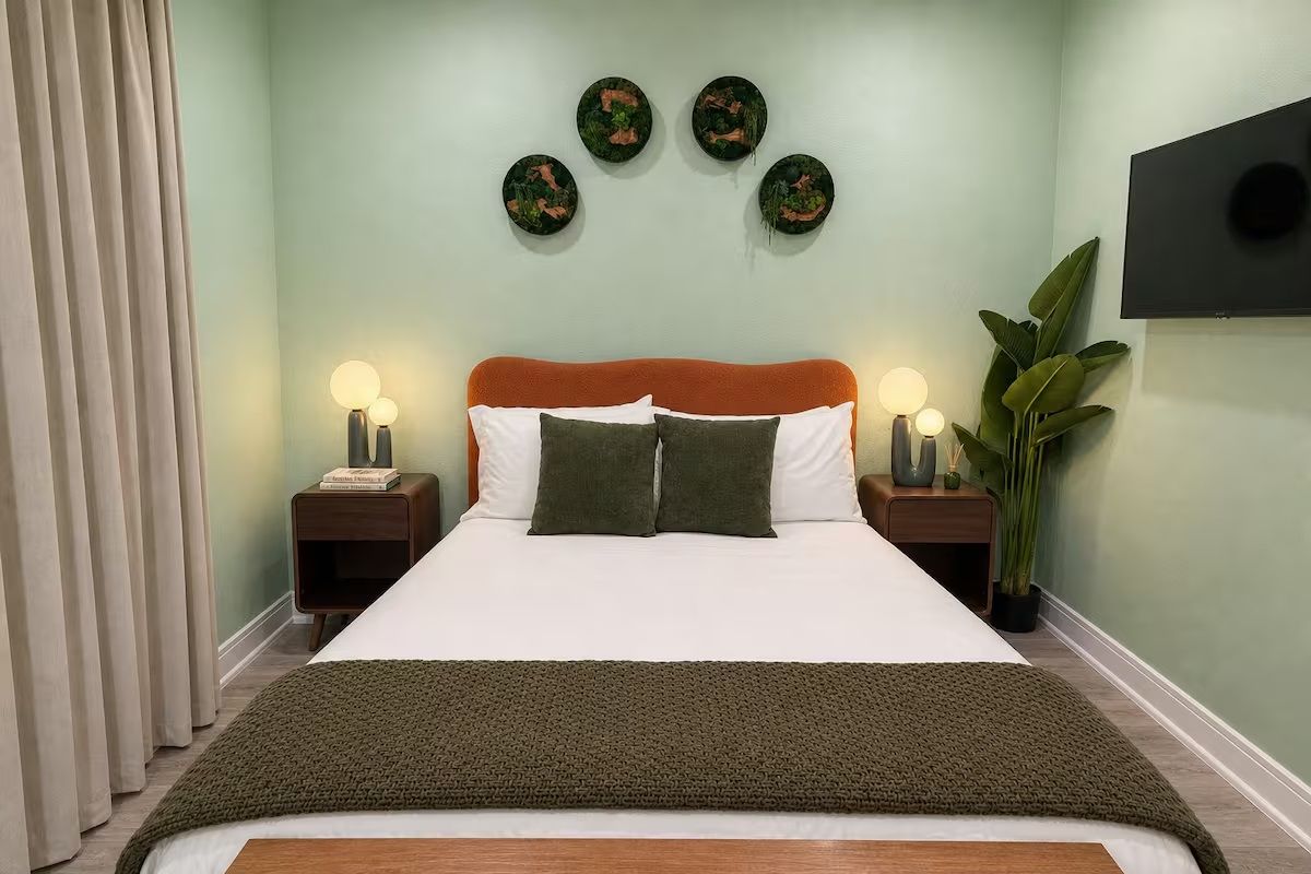 Quarto com cama, duas mesas de cabeceira, uma grande planta em vaso e obras de arte penduradas na parede.