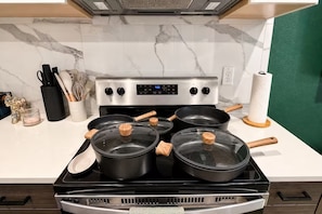A kitchen with a stainless steel stove, four pots with wooden handles, a white countertop, and a green wall. - Biophilic Oasis Knox Henderson (Dallas)