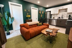 A living room with a sofa, a coffee table, and a kitchen area with cabinets and appliances. - Biophilic Oasis Knox Henderson (Dallas)