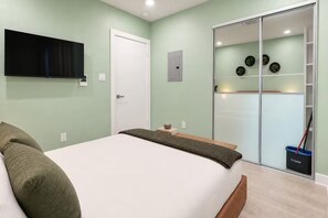 A bedroom with a bed, a television mounted on the wall, a door, and a sliding glass closet with decorative plates. - Biophilic Oasis Knox Henderson (Dallas)