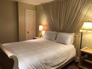 Een slaapkamer met een bed, twee bedlampen, een deur en een nachtkastje.