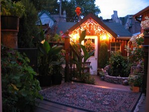 Een goed verlichte tuin met een tuinhuisje, planten in potten en een kamerkleed met patroon.
