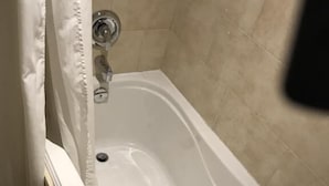 A white bathtub with a chrome faucet in a bathroom with beige tiled walls. - The Willow House Toronto (Toronto)
