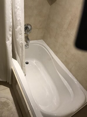 Een wit bad met een chromen kraan in een badkamer met beige betegelde wanden.