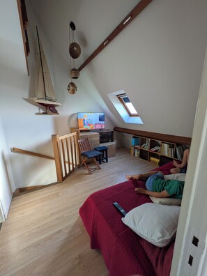 A loft bedroom with a sloped ceiling, a sailboat model, a television, a bookshelf, and a red bedspread. - Perfect 3-bedroom 2 bathroom apartment right on the waterfront (Wimereux)