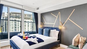 A modern hotel room with a large bed, a view of the city, and a geometric wall design. - Eastgate Urban Suites (Toronto)