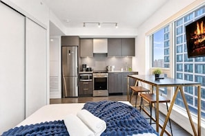 Een moderne hotelkamer met een bed, een eettafel, een keukenhoek en een groot raam met uitzicht op de stad.
