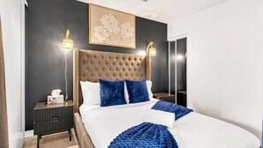 A modern bedroom with a tufted headboard, a large bed, two bedside tables, and a nightstand. - Eastgate Urban Suites (Toronto)