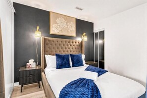 Een moderne slaapkamer met een gestoffeerd hoofdeinde, een groot bed, twee nachtkastjes en een bijzettafeltje.