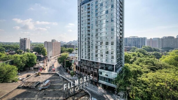 A modern hotel with a glass facade, surrounded by greenery and other buildings. - Eastgate Urban Suites (Toronto)
