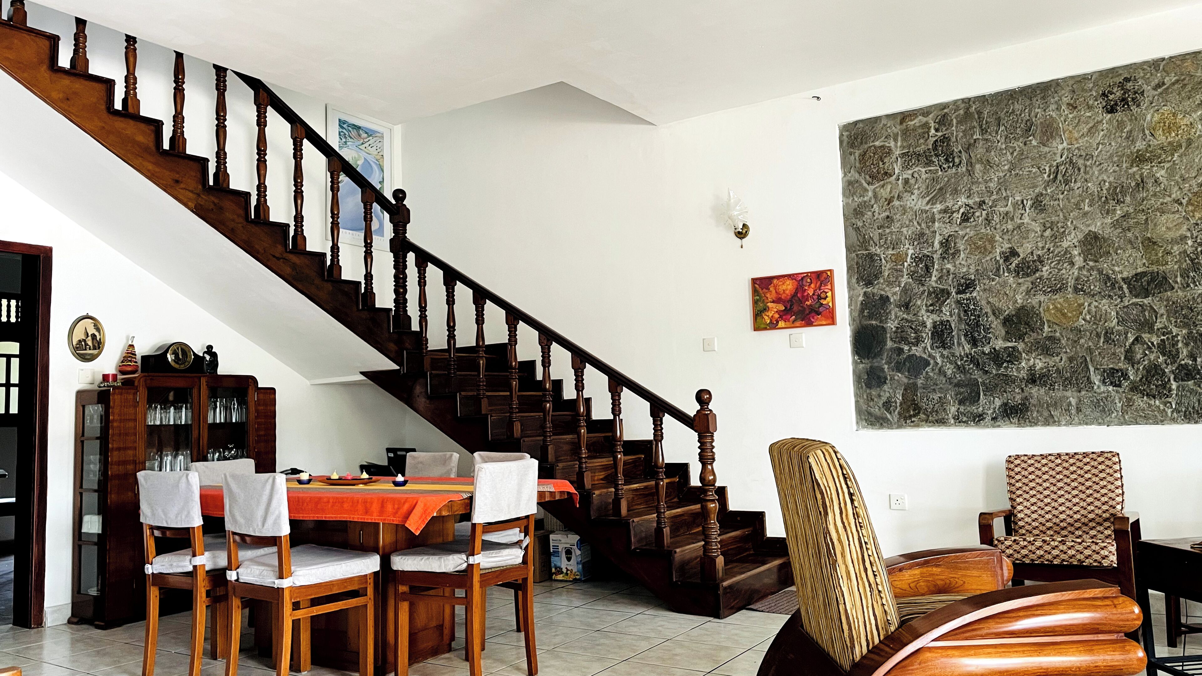 A dining area with a wooden staircase, a table set for two, and a large abstract painting on the wall.