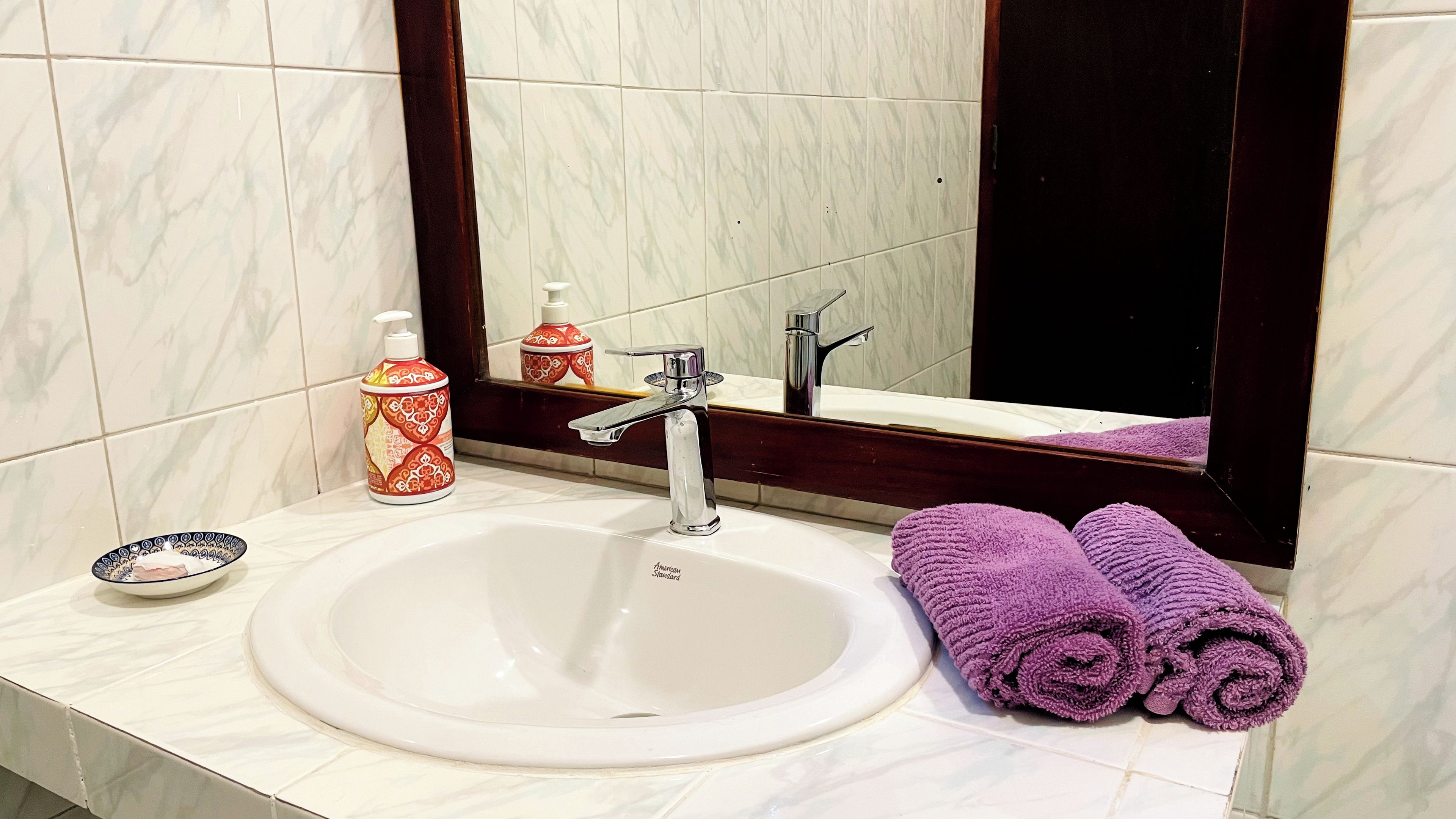 Un bagno con un lavandino bianco, uno specchio, un rubinetto, un dispenser di sapone e due asciugamani arrotolati.