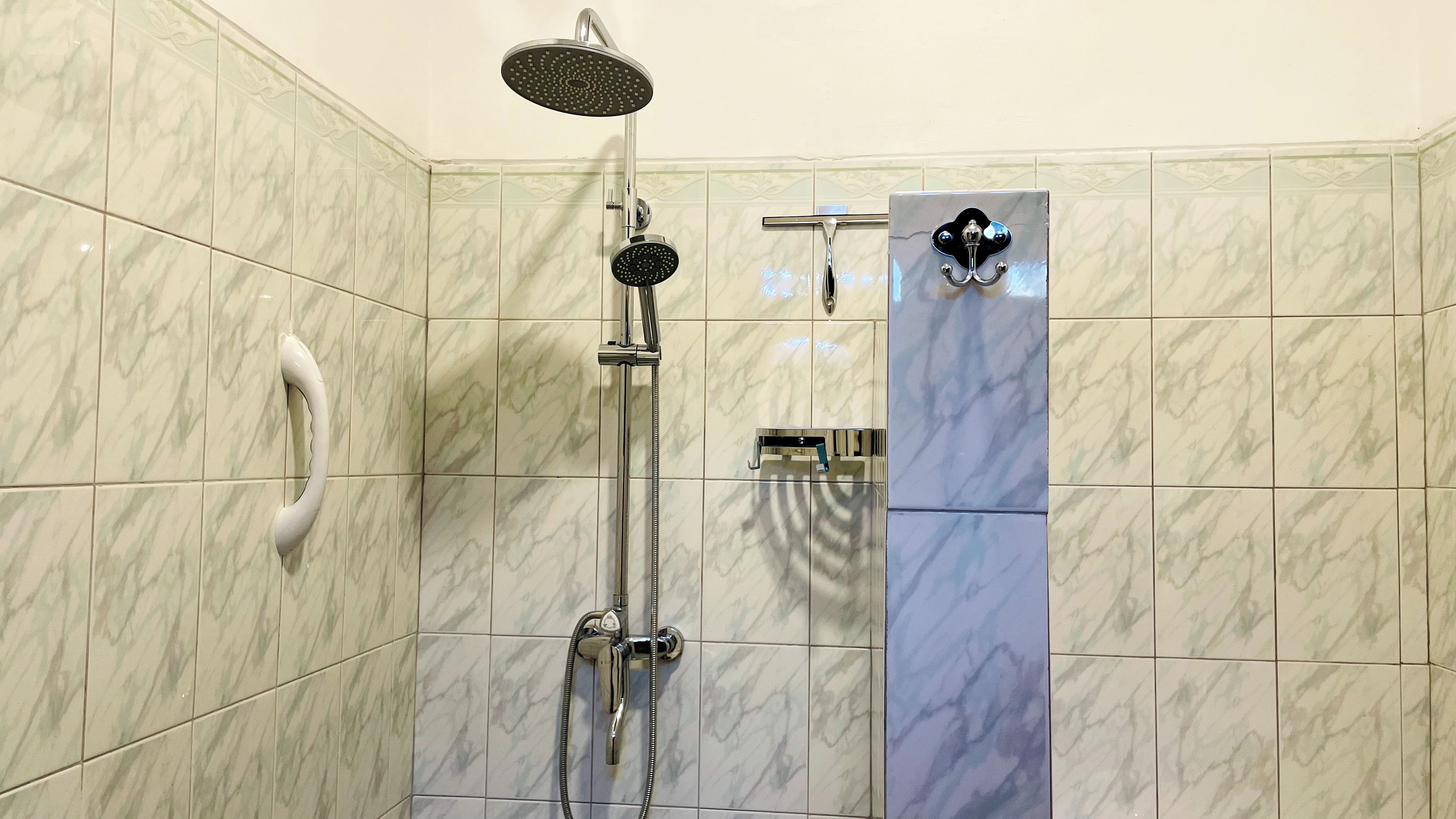Une douche équipée d’un pommeau de douche à main, d’un robinet mural et d’un panneau de commande.