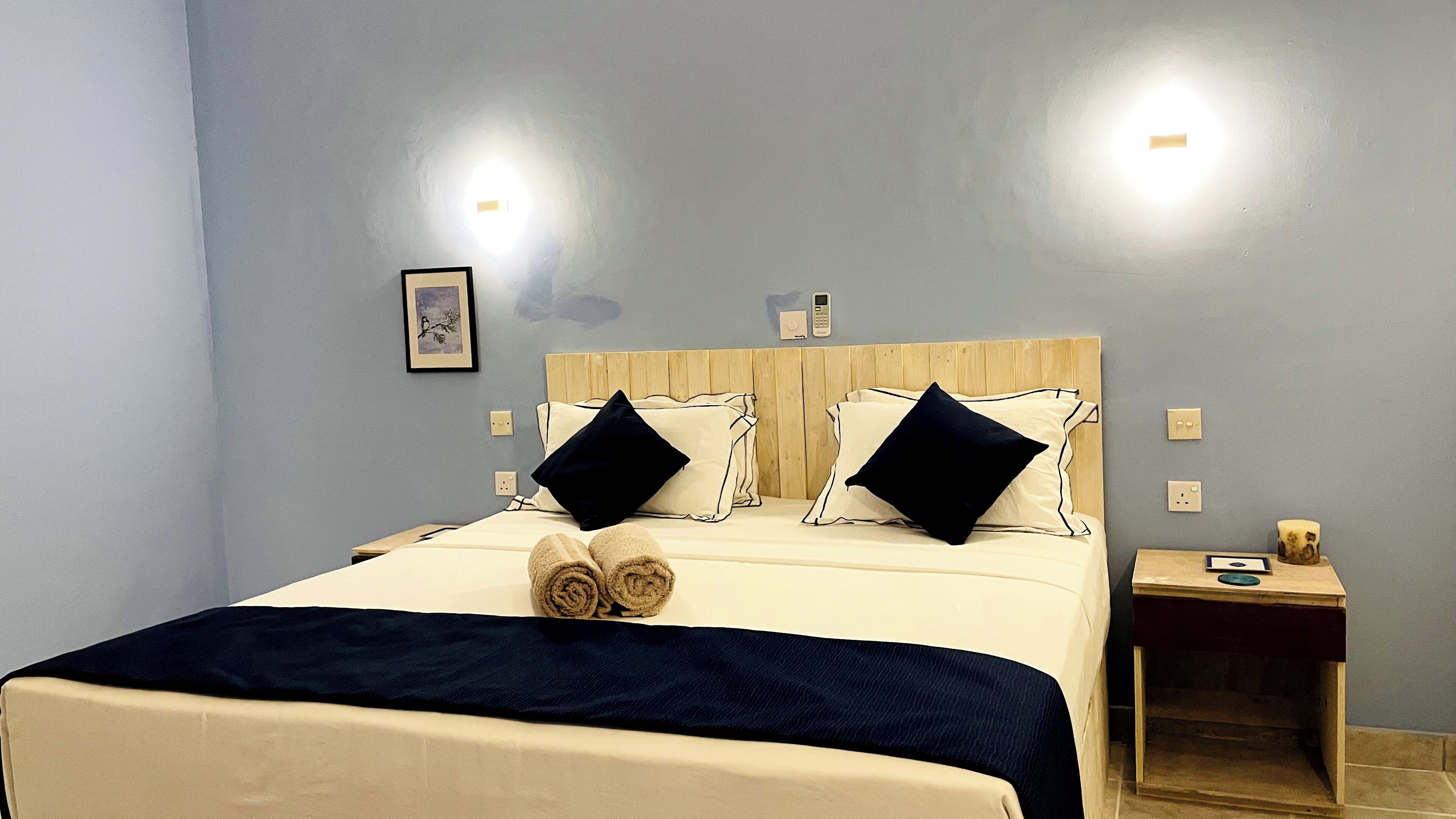A hotel room with a bed, two bedside tables, a wall-mounted phone, and a framed picture.