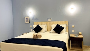A hotel room with a bed, two bedside tables, a wall-mounted phone, and a framed picture.