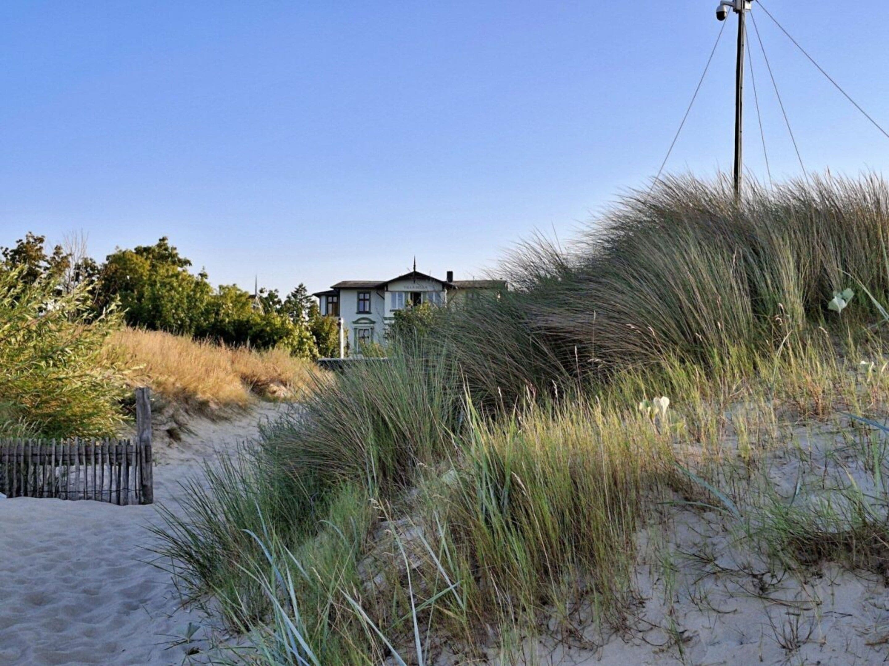Ein Küstenhaus mit sandigem Strand und Dünen im Vordergrund.